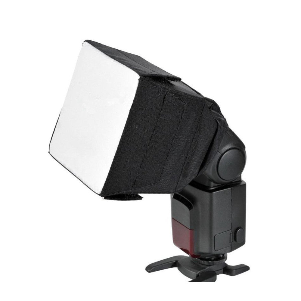 Black camera flash with white diffuser softbox attached, shown from a three-quarter side view against white background.
