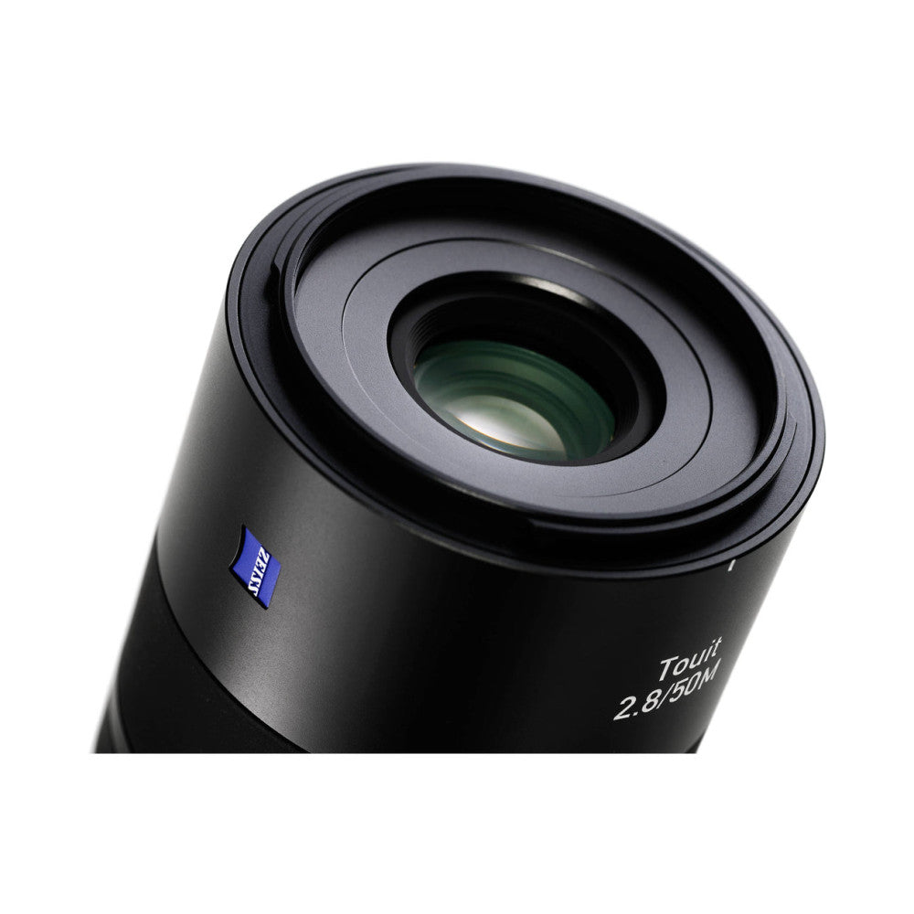 Close-up angled view of Zeiss Touit 50mm f/2.8 macro lens showing front element and barrel with blue Zeiss badge.
