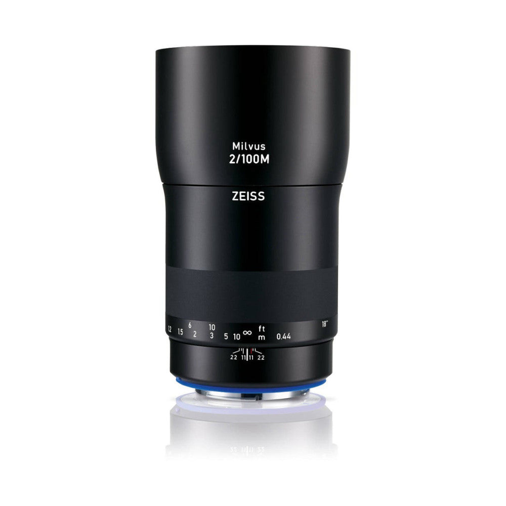 Black cylindrical camera lens shown from front view against white background, displaying Zeiss branding and Milvus 2/100M designation with focus ring and depth-of-field markings visible.
