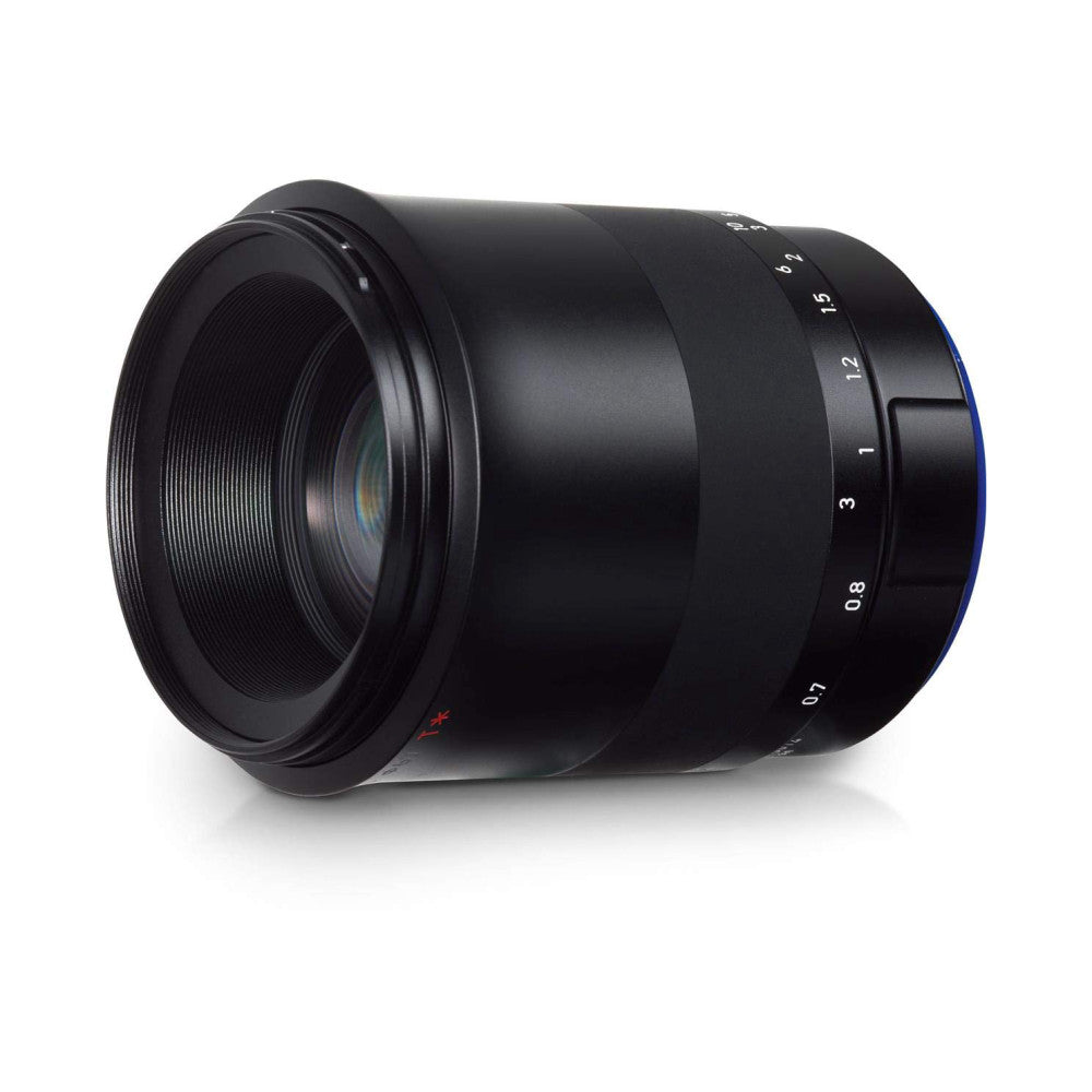 Black Zeiss Milvus macro lens shown from a side angle, displaying the focus ring with distance markings and lens elements visible through the front glass.