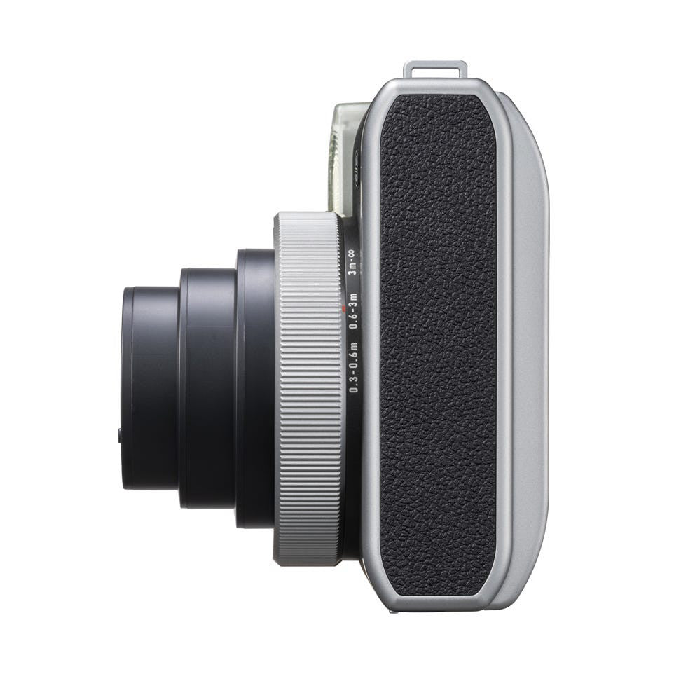 Side profile view of Fujifilm Instax Mini 99 silver instant camera showing lens barrel, focusing ring, and textured back panel.