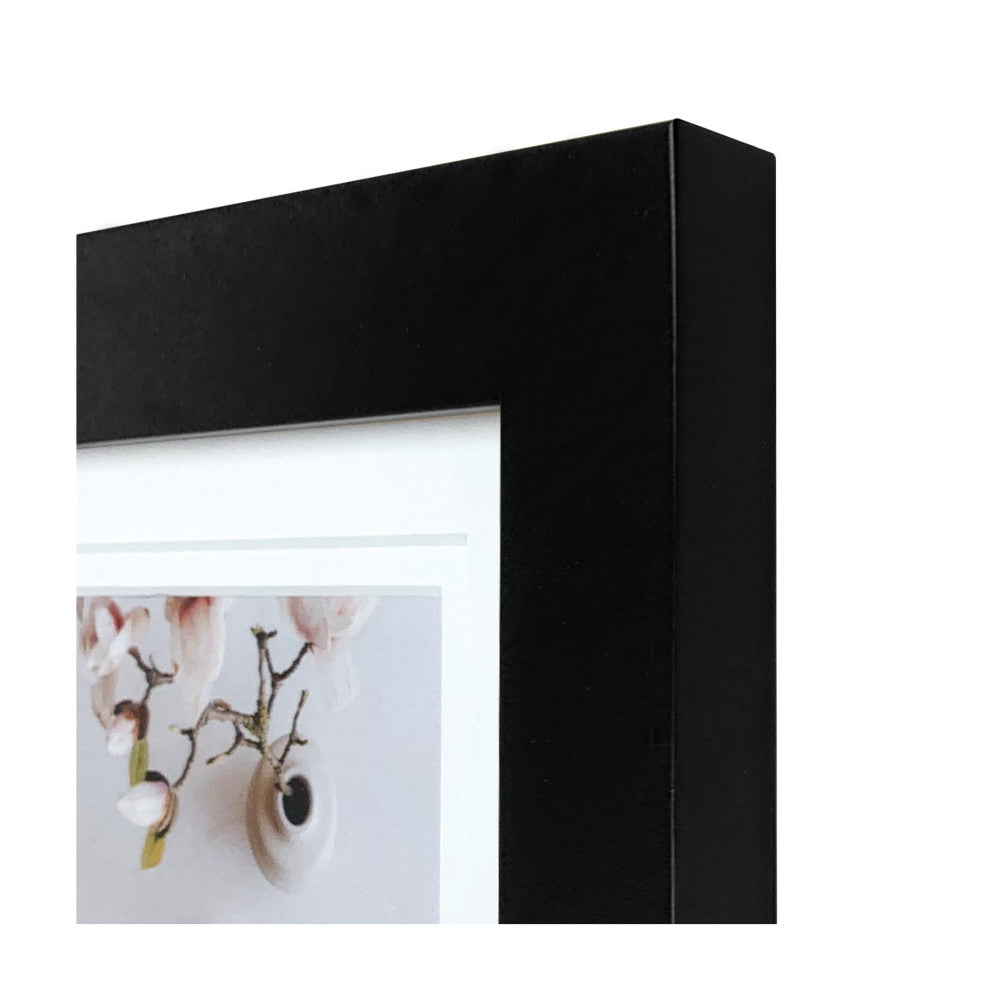 Close-up detail of black picture frame corner showing deep matte finish and white mat board with partial view of framed botanical artwork.