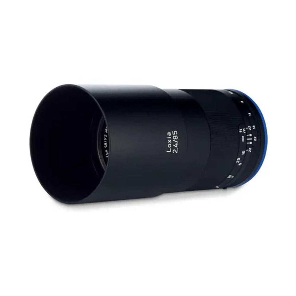 Zeiss Loxia 85mm f/2.4 lens shown from the side at an angle, displaying the barrel with focus ring and depth-of-field markings, with lens hood attached.