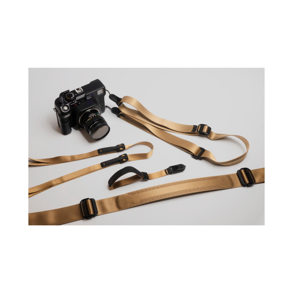 Flat lay of Peak Design Cuff camera strap in coyote tan showing multiple strap variations with black hardware and a vintage camera body.