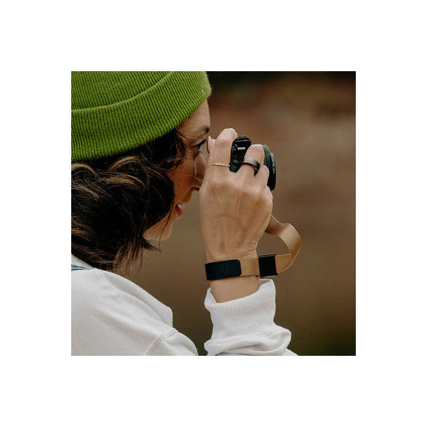 Person wearing green beanie photographing with camera secured by Peak Design cuff strap on wrist, shown from behind in active use.