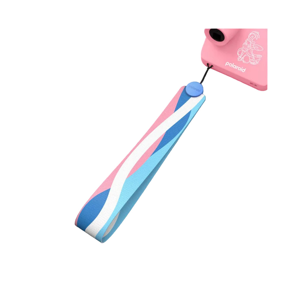 Pink Polaroid GO camera with Sylveon design shown at angle above a striped wrist strap in pink, blue, and white colors against black background.