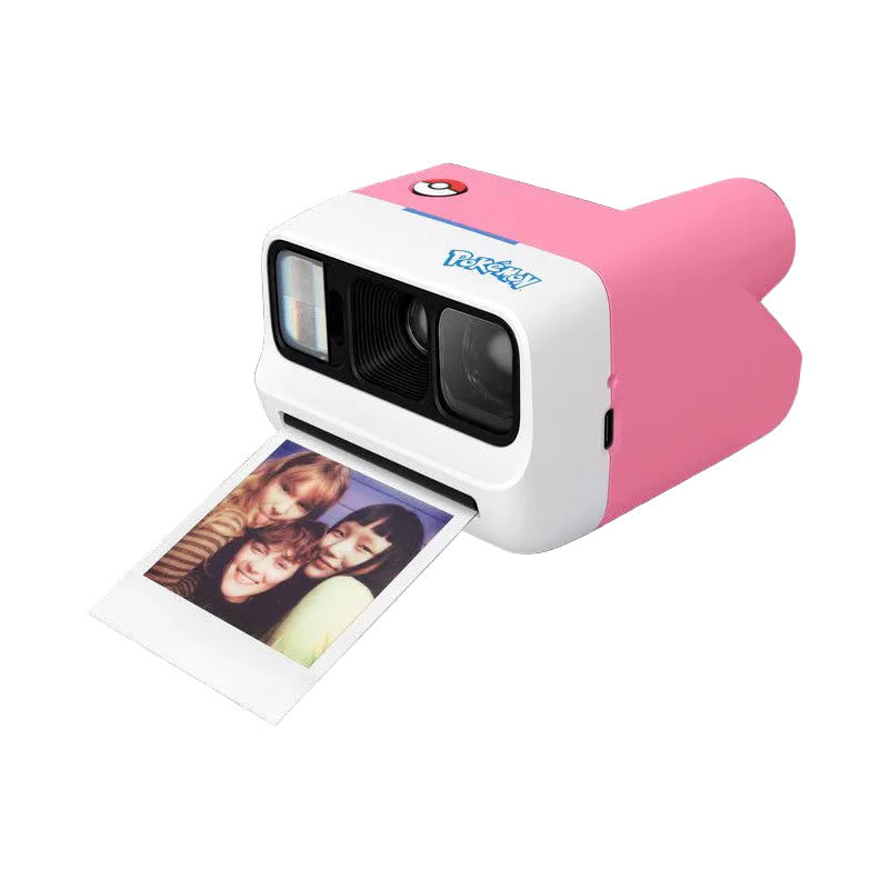 Pink and white instant camera with dual lens shown at three-quarter angle, ejecting a printed photo of three people against black background.