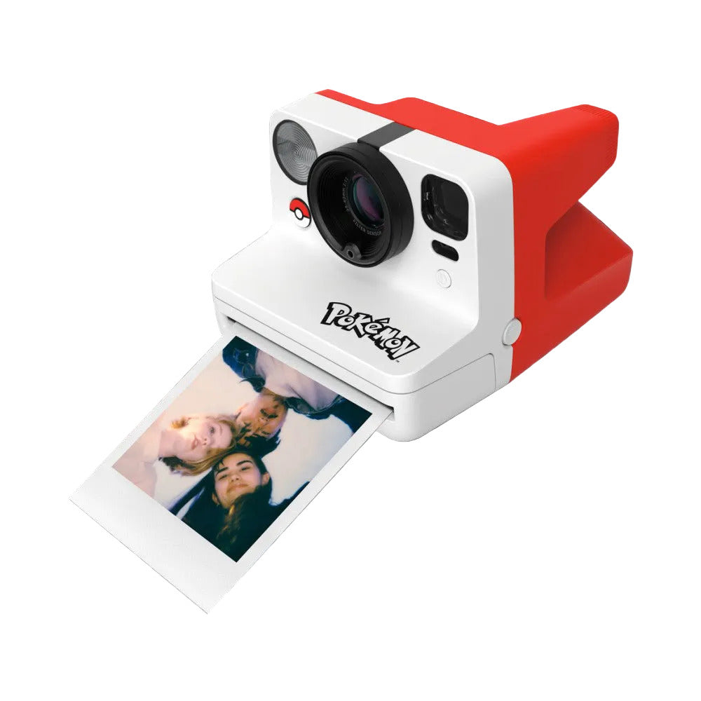 White and red instant camera with Pokéball logo, shown at an angle with printed photo emerging from the bottom slot, against a black background.