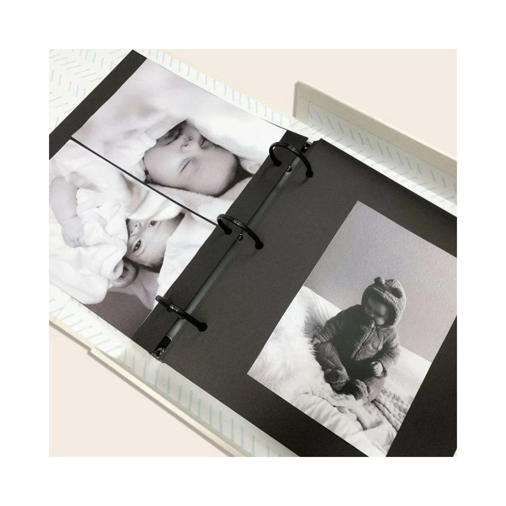 Black binder with black metal rings open to display black and white photos of babies and children on white pages, overhead view.