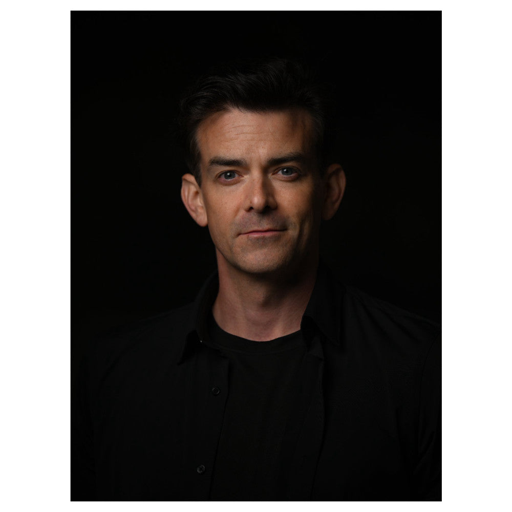 Professional portrait photograph of a man against a dark background, lit with studio lighting