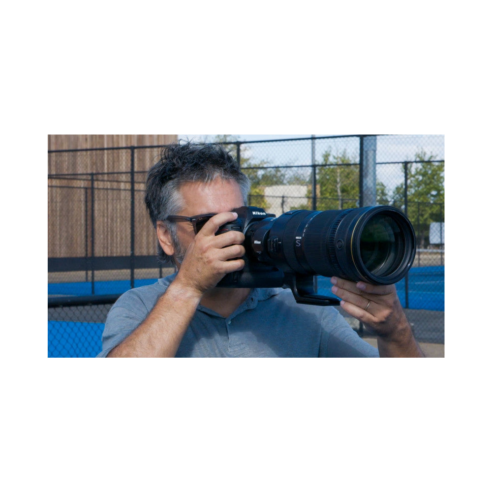 Photographer holding Nikon Z camera with NIKKOR Z 120-300mm telephoto lens, demonstrating in-use grip and size at outdoor sports facility.