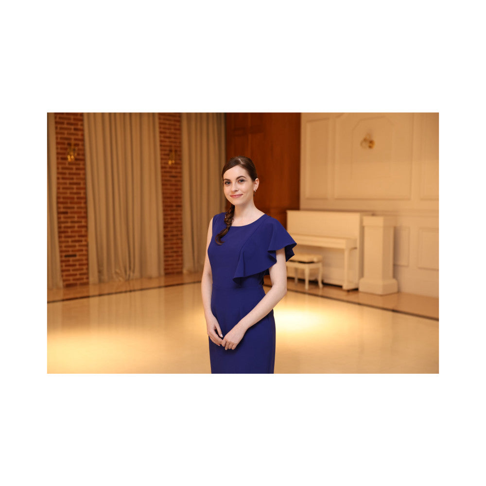 Woman in navy blue dress standing in an elegant interior space with warm lighting and classical architectural details.