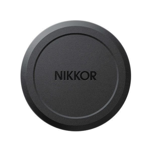 Front view of a black circular lens cap with "NIKKOR" text embossed in the center, shown against a white background.