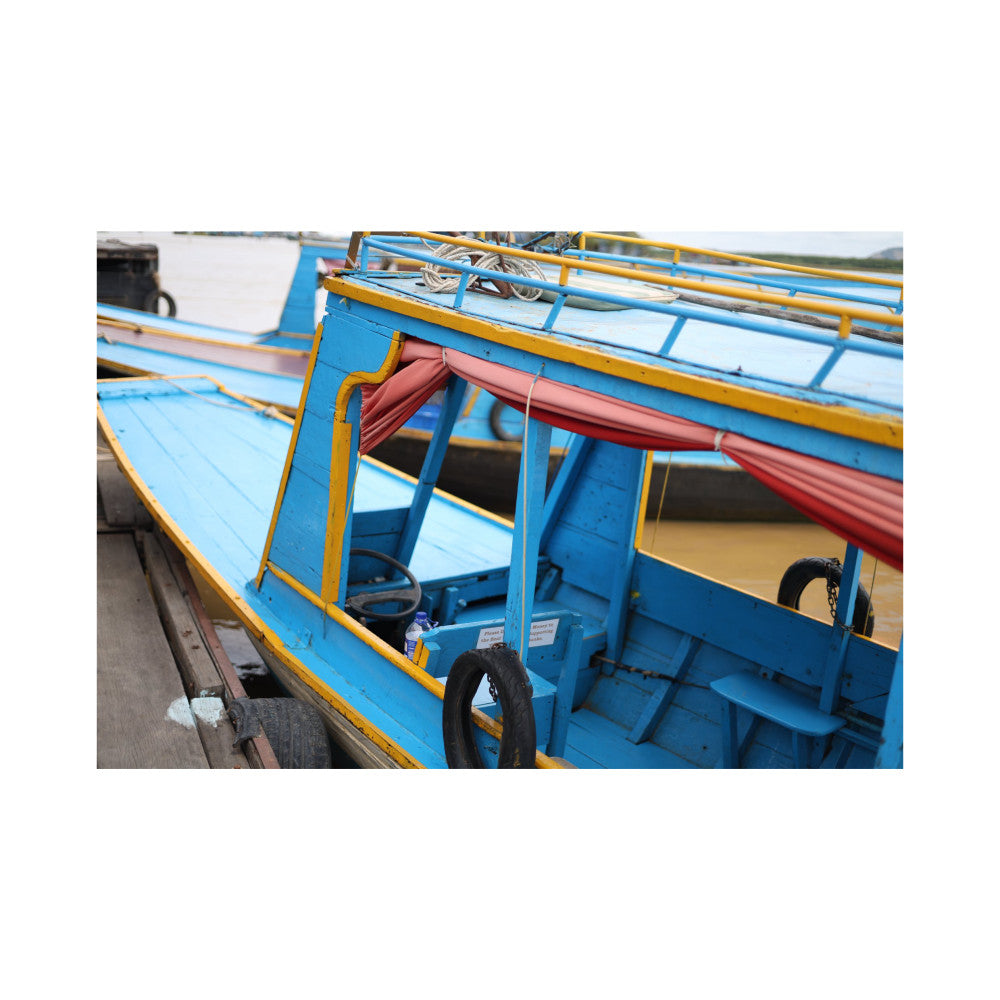 Colorful blue and yellow wooden fishing boats docked at water's edge with red canvas canopy and black tire bumpers visible.