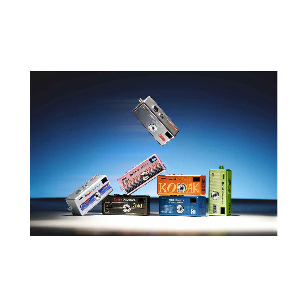 Six colorful miniature Kodak Charmera cameras displayed against a blue gradient background, including silver, white, pink, black, orange, blue, and green models, with one floating above the group.