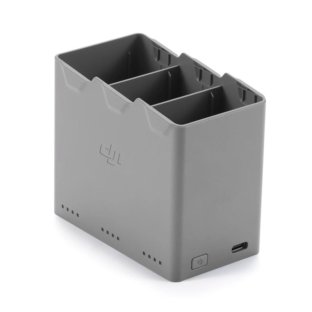 Gray DJI charging hub with three compartments shown from angled front view, displaying USB-C port and power button on lower front.