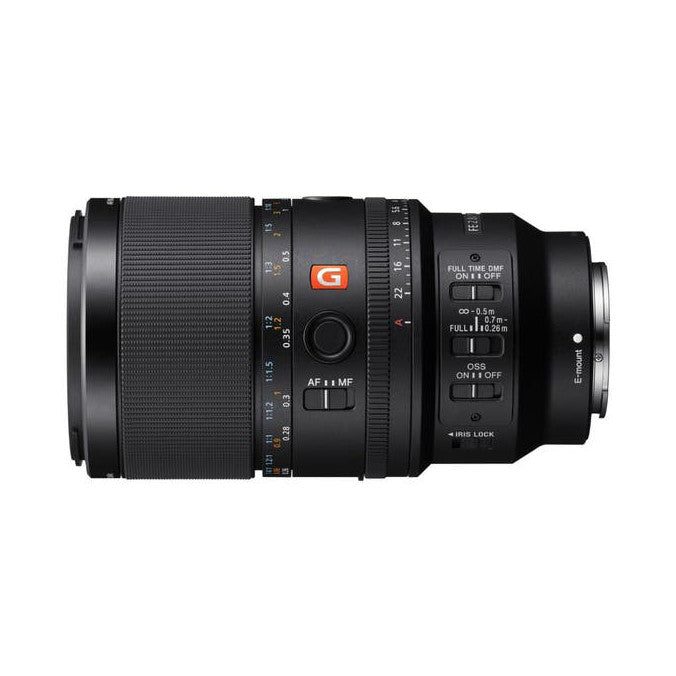 Side view of Sony FE 100mm f/2.8 Macro GM OSS lens showing focus ring, AF/MF switch, and stabilization controls on black barrel.