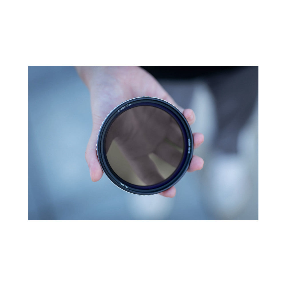 Hand holding a circular camera filter showing its dark tinted glass and labeled rim against a blurred outdoor background.