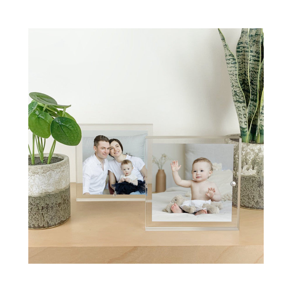 Two clear acrylic photo frames displayed on a wooden shelf with potted plants, showing family photos in an in-use lifestyle setting.