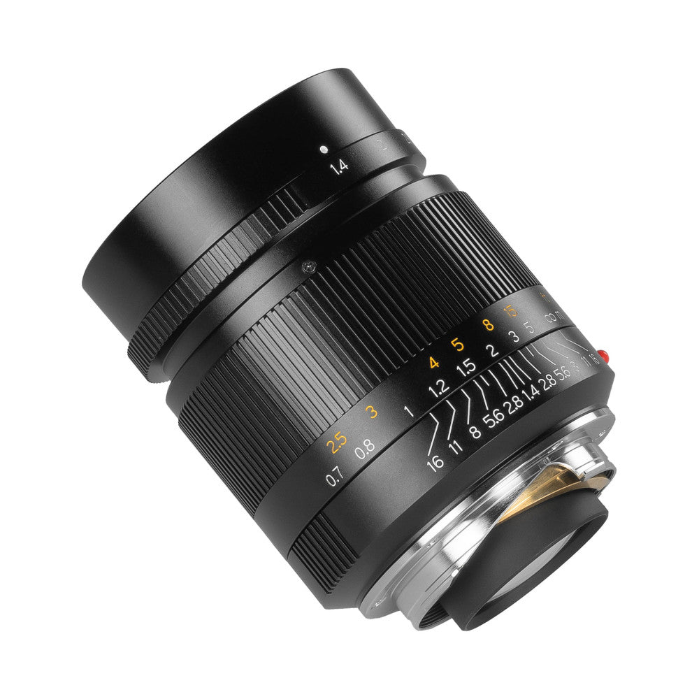 Black manual focus 28mm f/1.4 lens tilted at angle against white background, showing focus ring and aperture markings.
