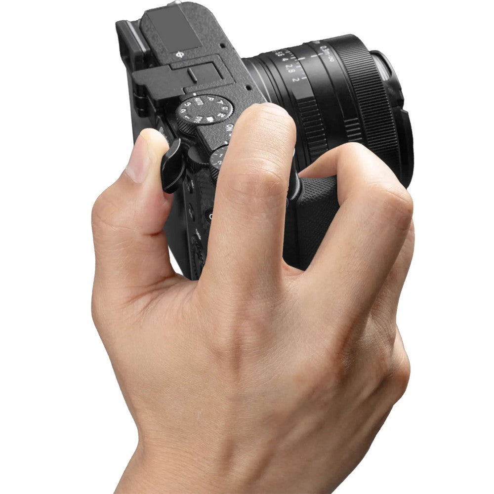 Hand holding a compact black camera with attached grip, shown from a three-quarter view demonstrating proper grip positioning.