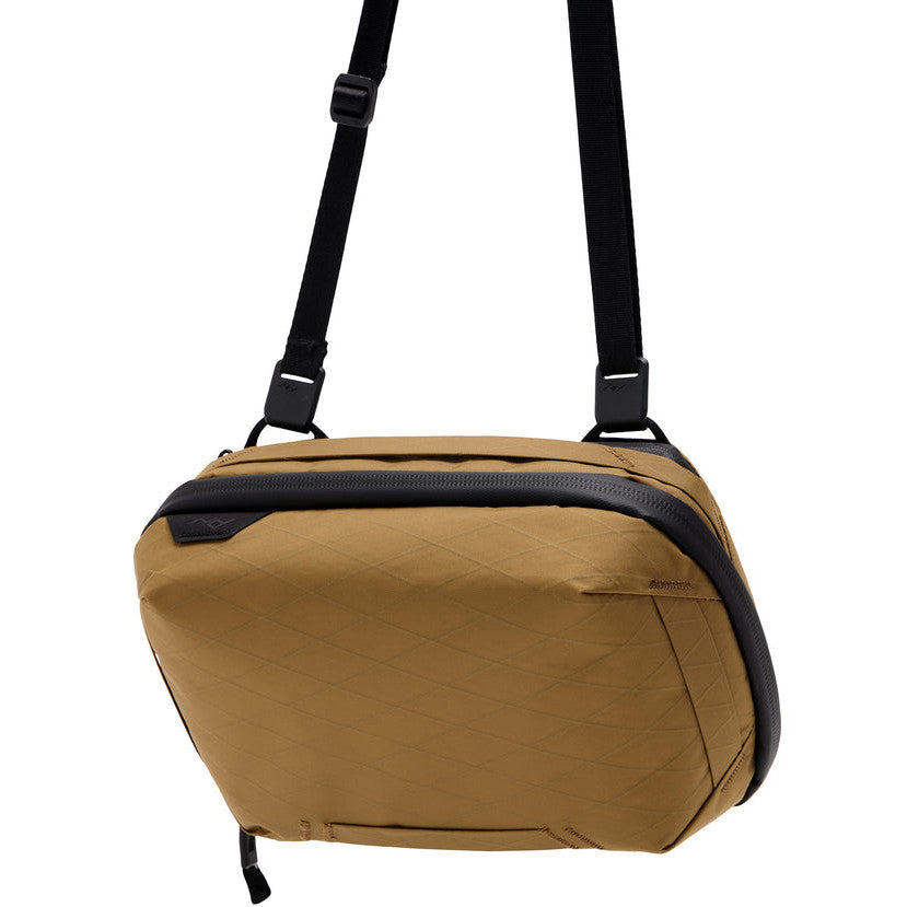 Coyote-colored Peak Design Tech Pouch 2L displayed against white background, showing front and top view with black shoulder straps and zipper details.