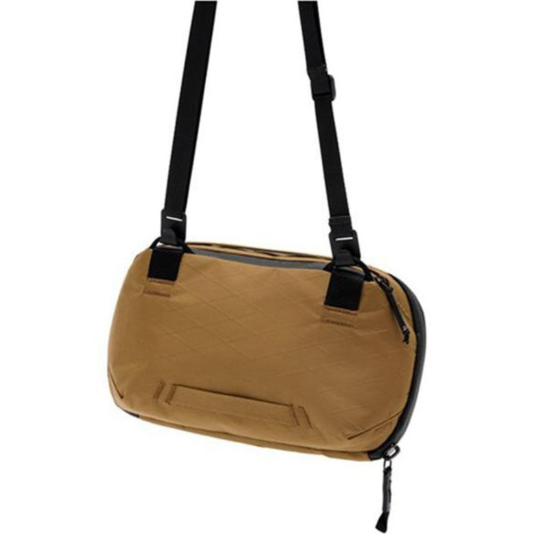 Coyote-colored Peak Design Tech Pouch 2L shown from front angle, suspended by black shoulder straps against white background.