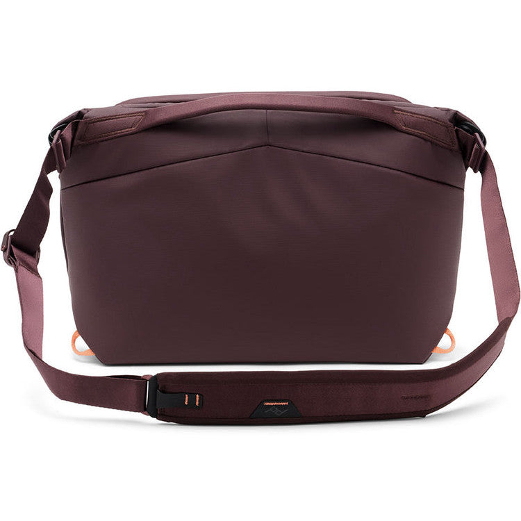 Rear view of a burgundy/eclipse colored sling bag with adjustable shoulder strap and orange accent details on the sides.