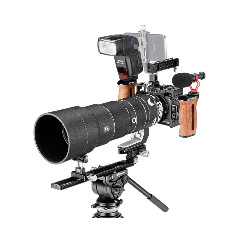 Professional camera cage setup with telephoto lens, flash, microphone, and phone mount on tripod, angled three-quarter view.