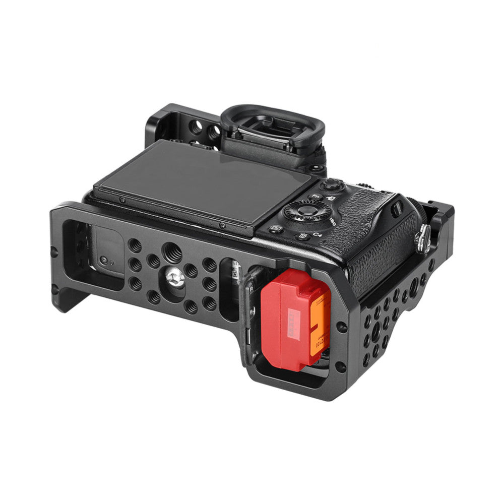 Black camera cage with red and orange battery grip mounted on Sony mirrorless camera with LCD screen visible, shown at three-quarter angle.