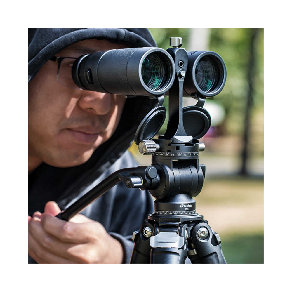 Person using binoculars mounted on tripod with Leofoto adapter, demonstrating in-use application outdoors.