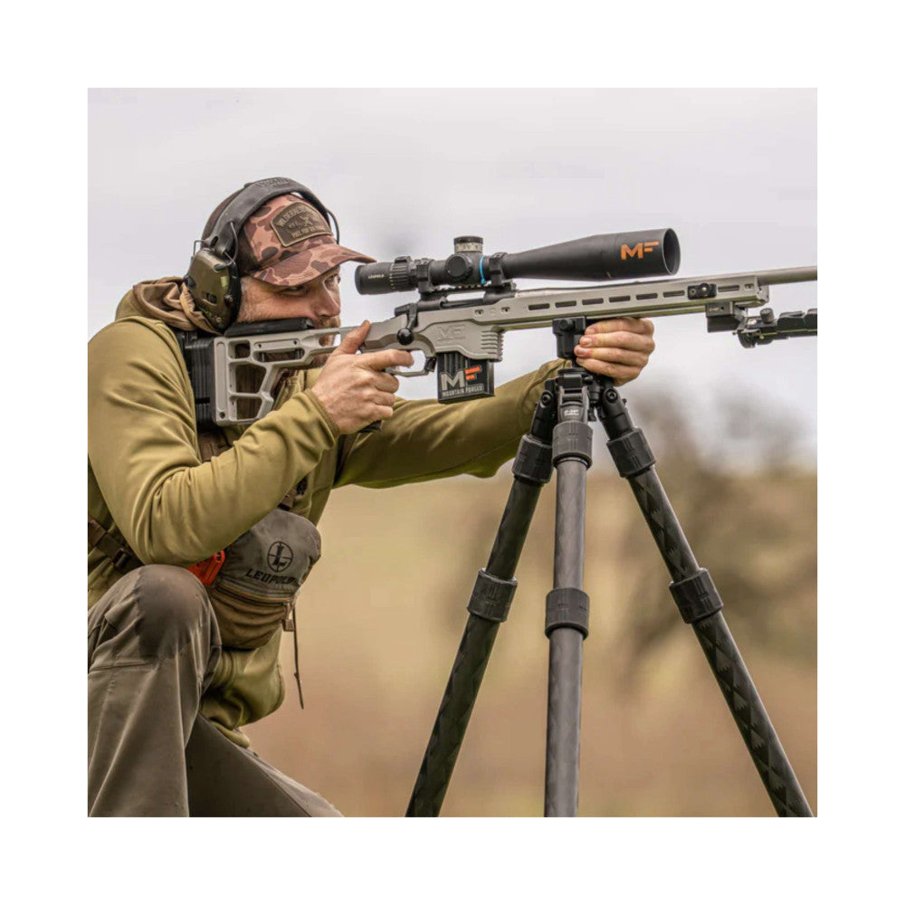 Shooter aiming rifle mounted on Leofoto tripod with scope, demonstrating in-use stability and durability in field conditions.