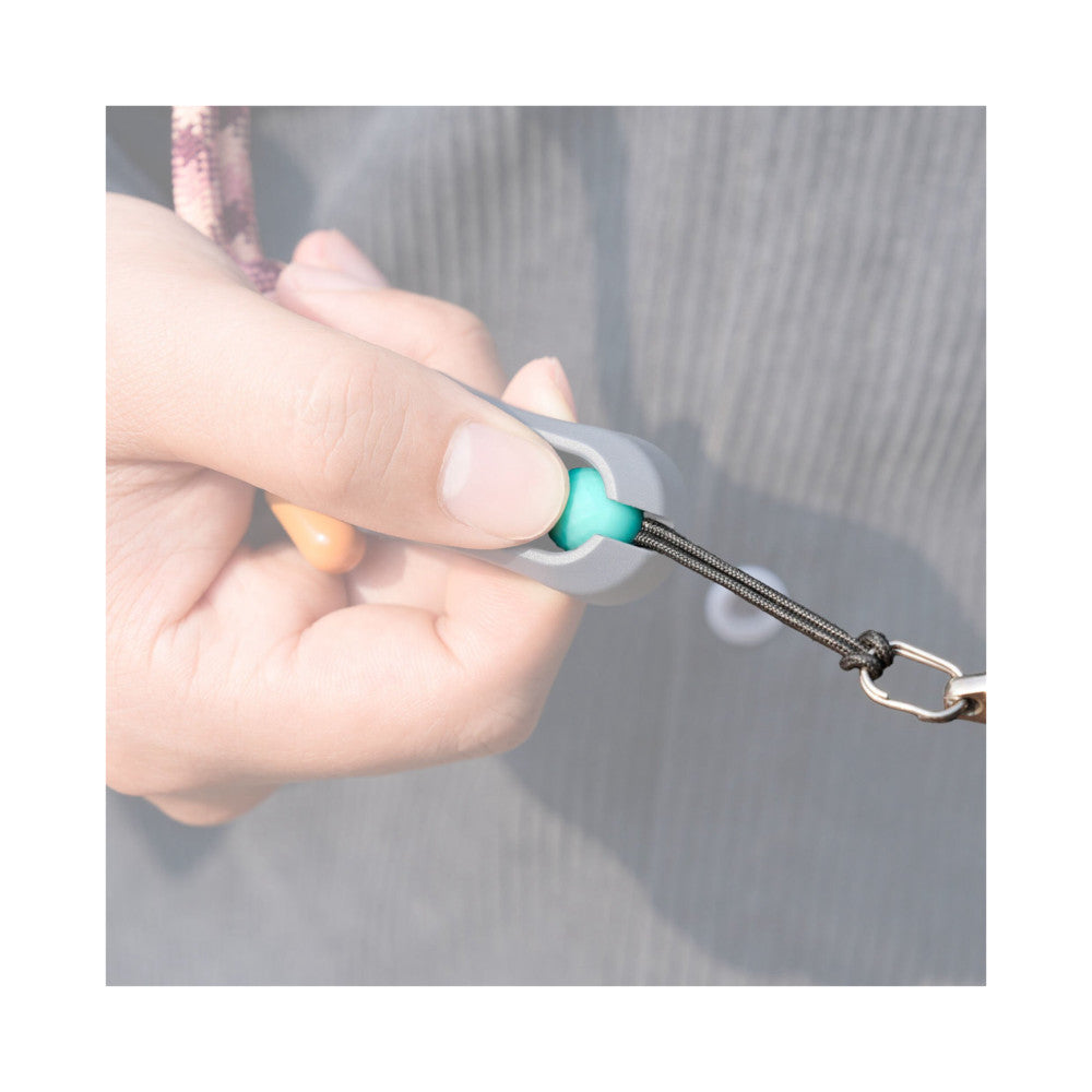 Hand holding gray quick-attach ball connector with turquoise detachable sphere and black braided camera strap with metal carabiner.
