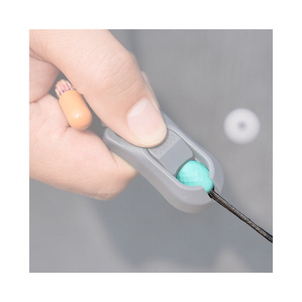 Close-up of hands demonstrating the turquoise quick-attach ball connector being inserted into a gray socket on a camera strap accessory.