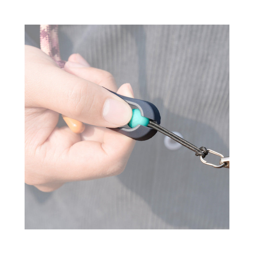 Close-up of hand holding black quick-attach strap connector with turquoise button and metal carabiner clip.
