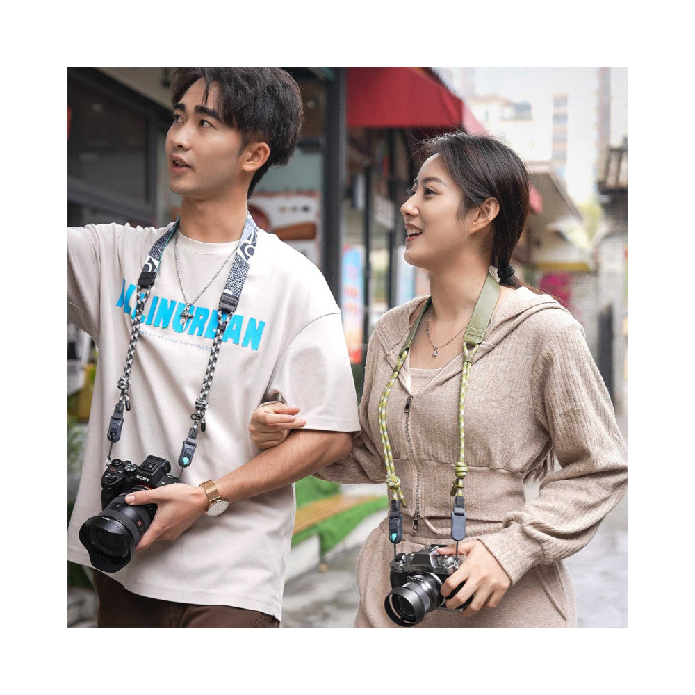 Two people wearing camera straps while holding cameras outdoors on a city street, demonstrating in-use product wear.
