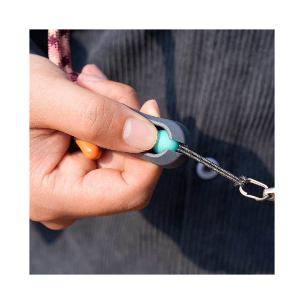 Close-up of hand holding camera strap connector showing turquoise attachment point and braided gray cord against dark clothing background.