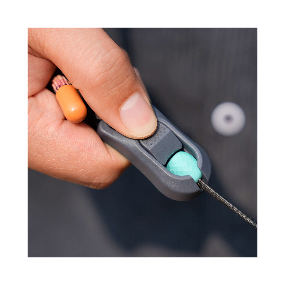 Close-up of a hand holding a grey camera strap connector with turquoise button detail and attached cord.