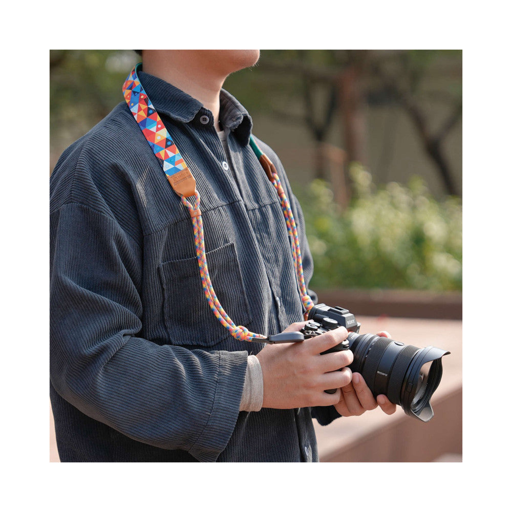 Person wearing colorful patterned camera strap attached to Sony camera, shown in-use from side angle in outdoor setting.