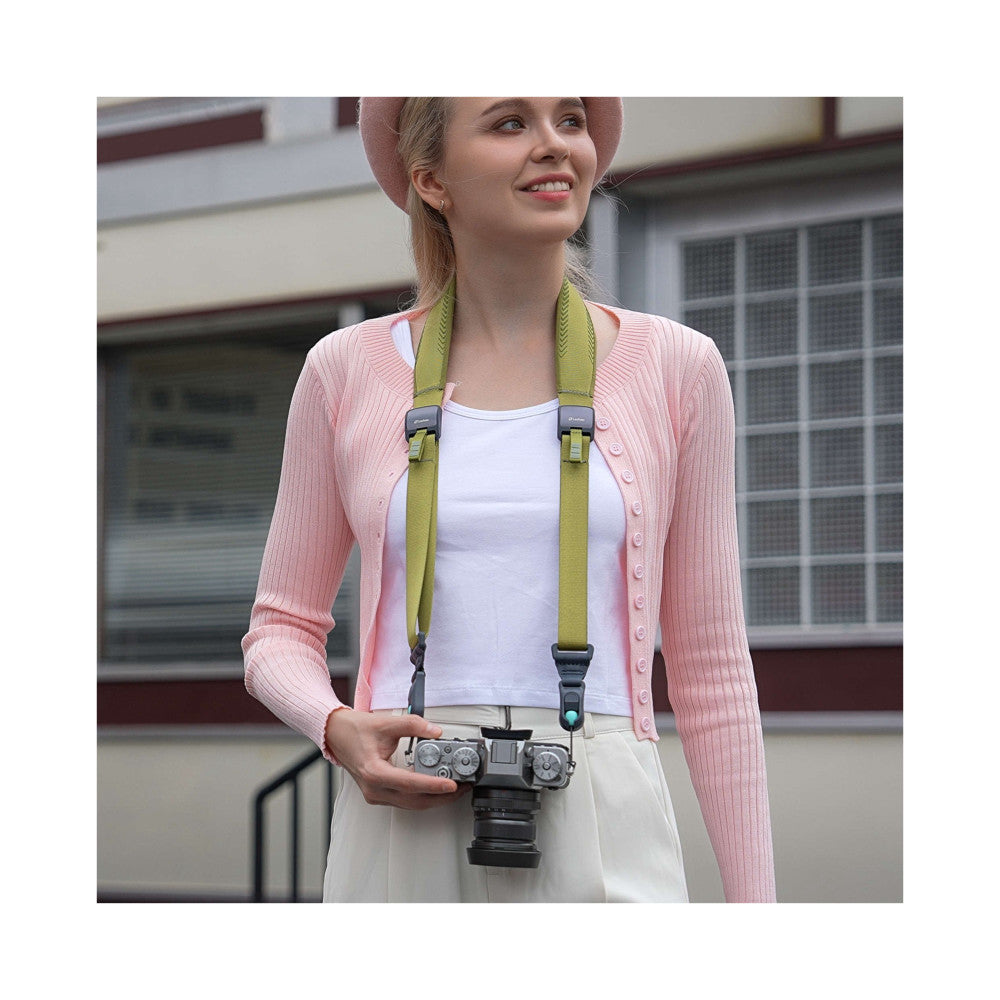 Woman wearing pine green camera strap with drone remote control, demonstrating in-use styling with pink cardigan and white hat.