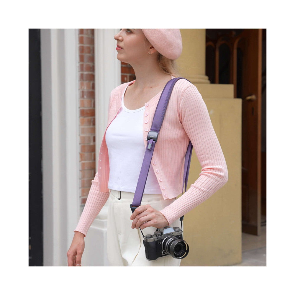 Woman wearing purple camera strap with vintage film camera, shown in-use at side angle against urban backdrop.