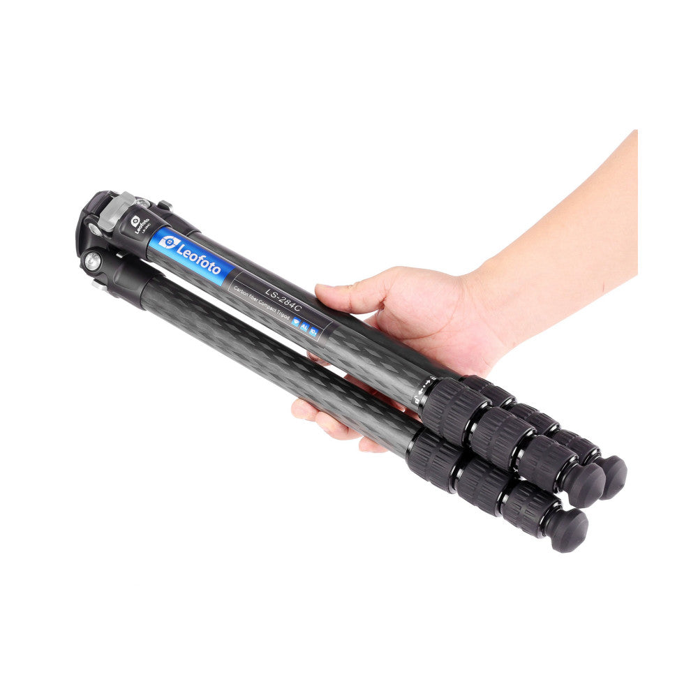 Hand holding extended Leofoto carbon fiber tripod legs with blue head and ball mount against white background.