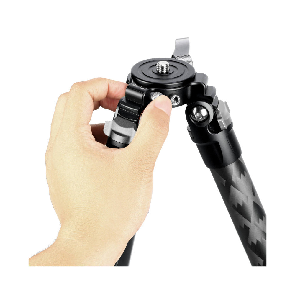 Hand holding the tripod head showing the ball mount, lever release mechanism, and patterned carbon fiber leg detail.