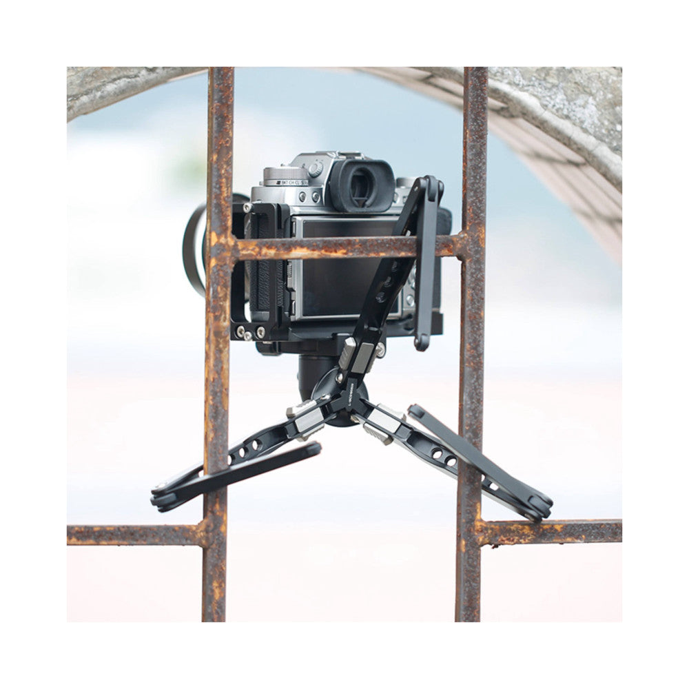 Leofoto MT-03 tripod with ball head supporting a vintage medium format camera, viewed through a rusty metal frame against a blurred outdoor background.
