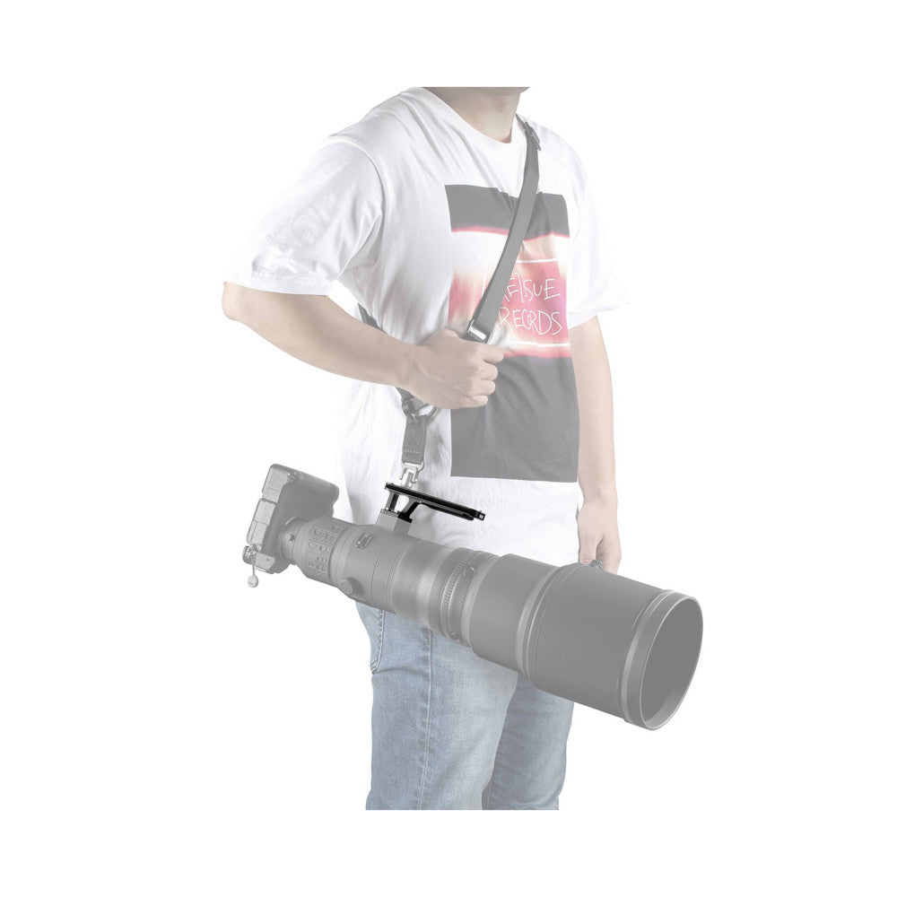 Person wearing white t-shirt holding large telephoto lens with attached Arca-type lens foot plate at hip level, demonstrating in-use positioning.
