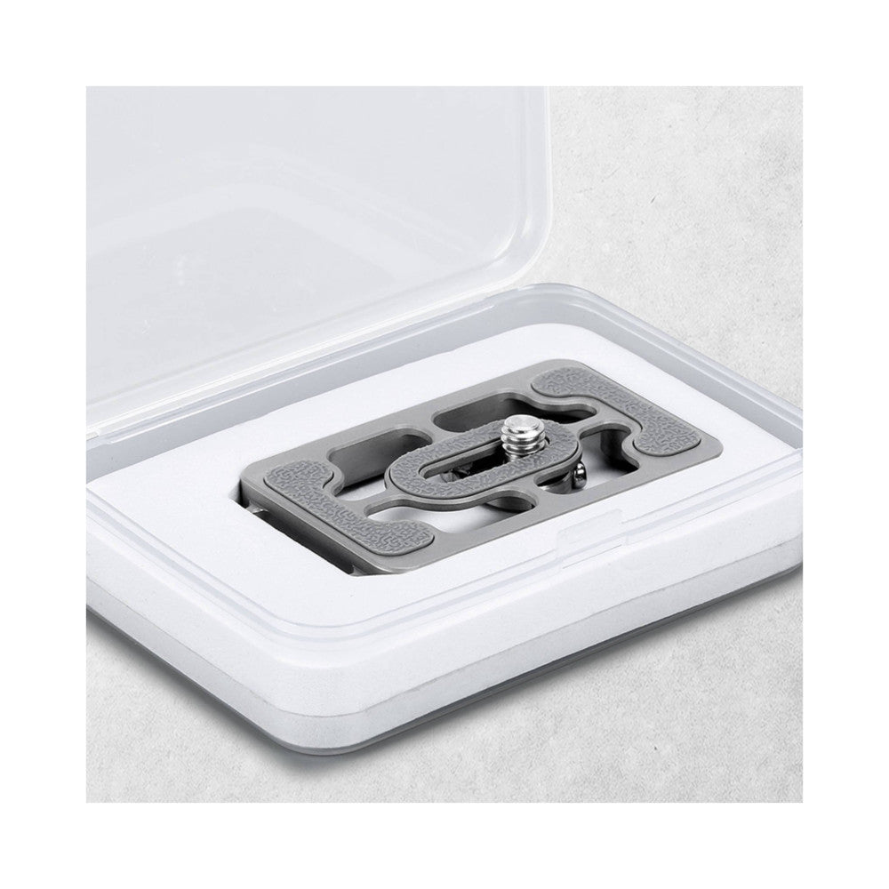 Top-down view of a gray titanium Arca Swiss quick release plate mounted in a white plastic case, showing the plate's textured surface and central screw mechanism.