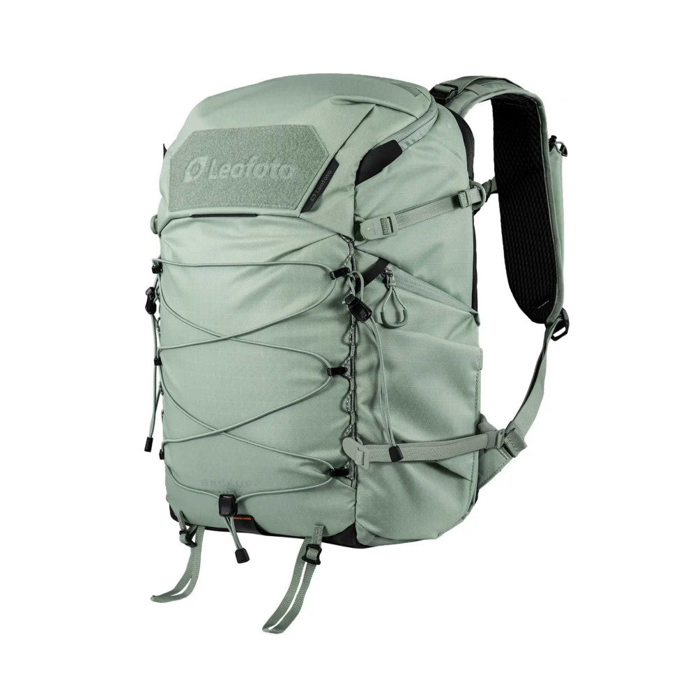 Front view of a green camera backpack with multiple external pockets, shoulder straps, and attachment points against a white background.