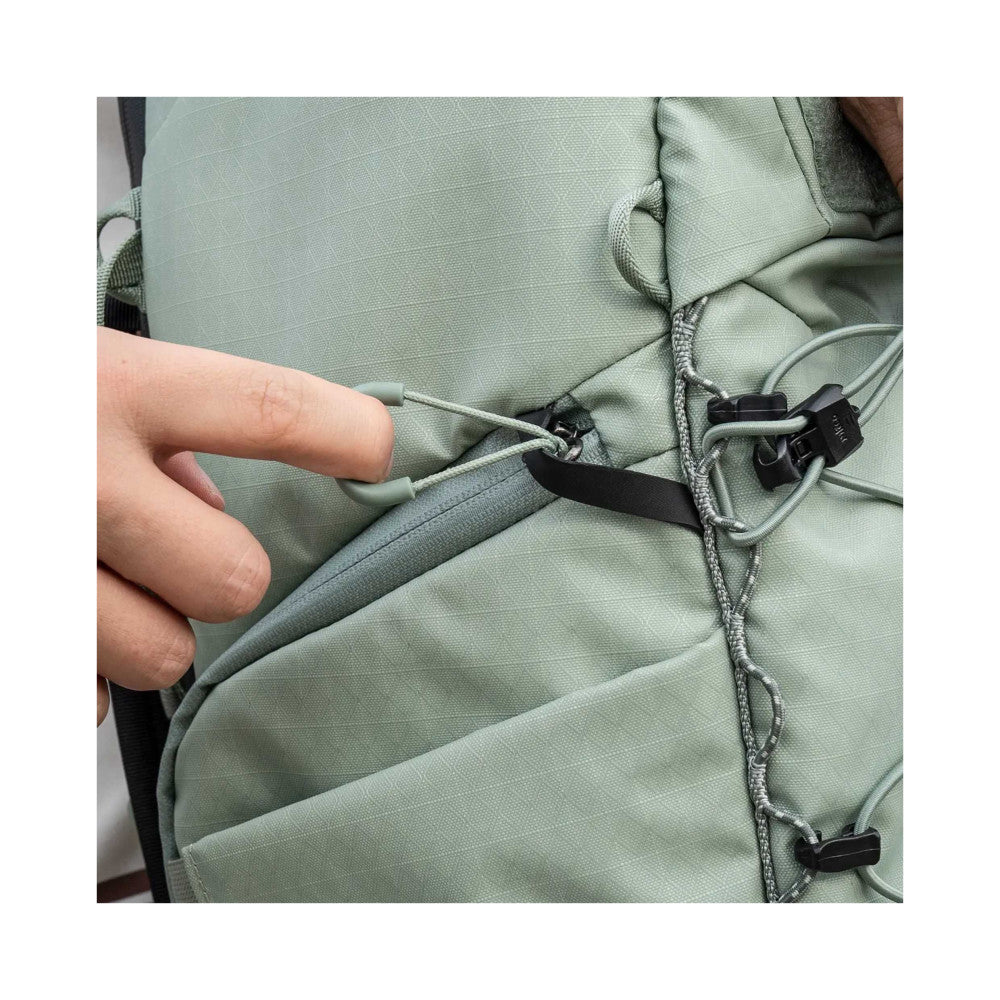 Close-up of green camera backpack showing compression straps with black plastic clips and cord attachments detail.