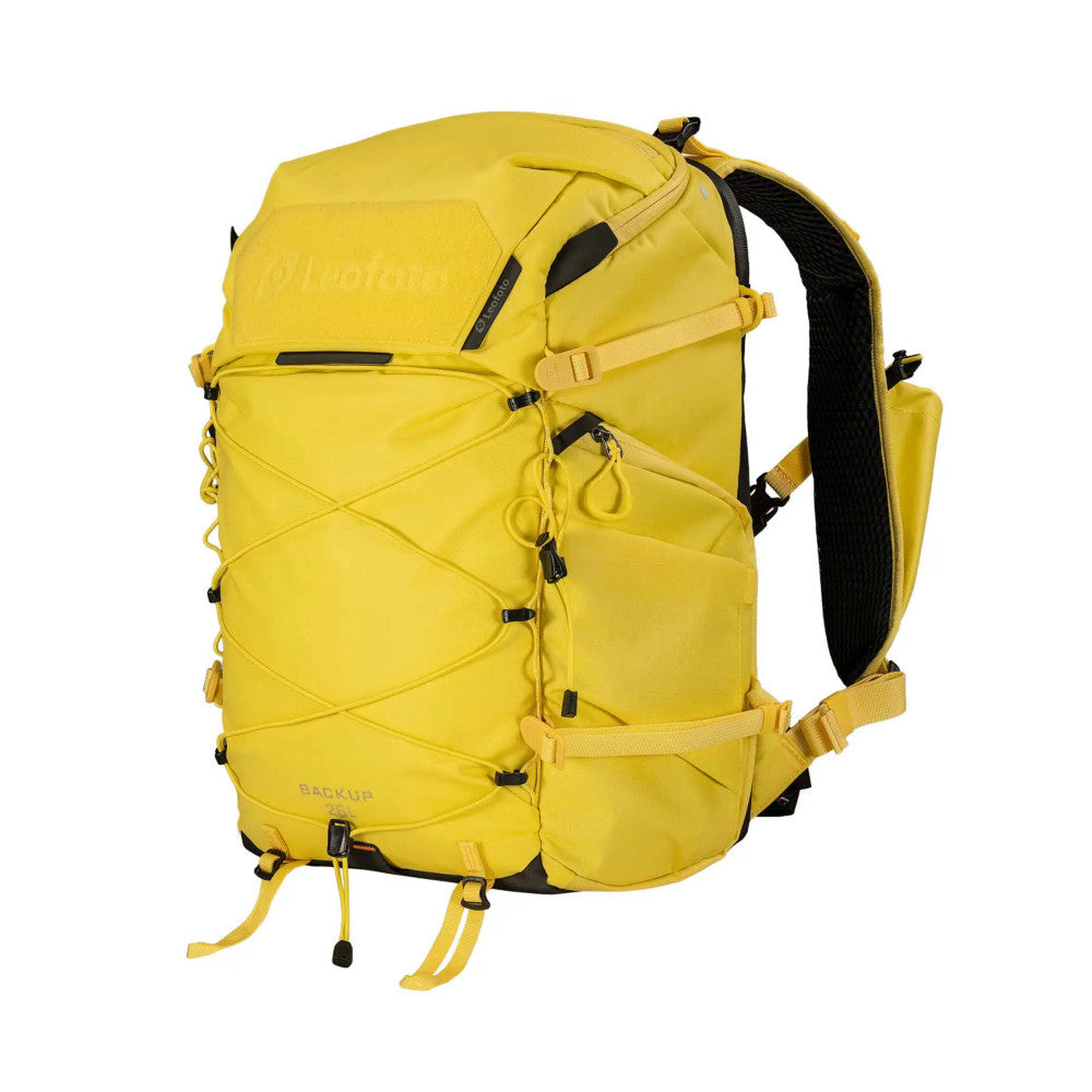 Front view of a bright yellow camera backpack with X-strap design, multiple compartments, and black mesh shoulder straps against a white background.