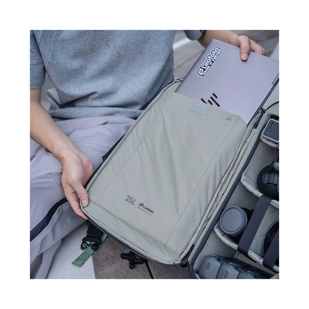 Person opening beige camera backpack showing interior compartments with photography equipment and lens caps visible.